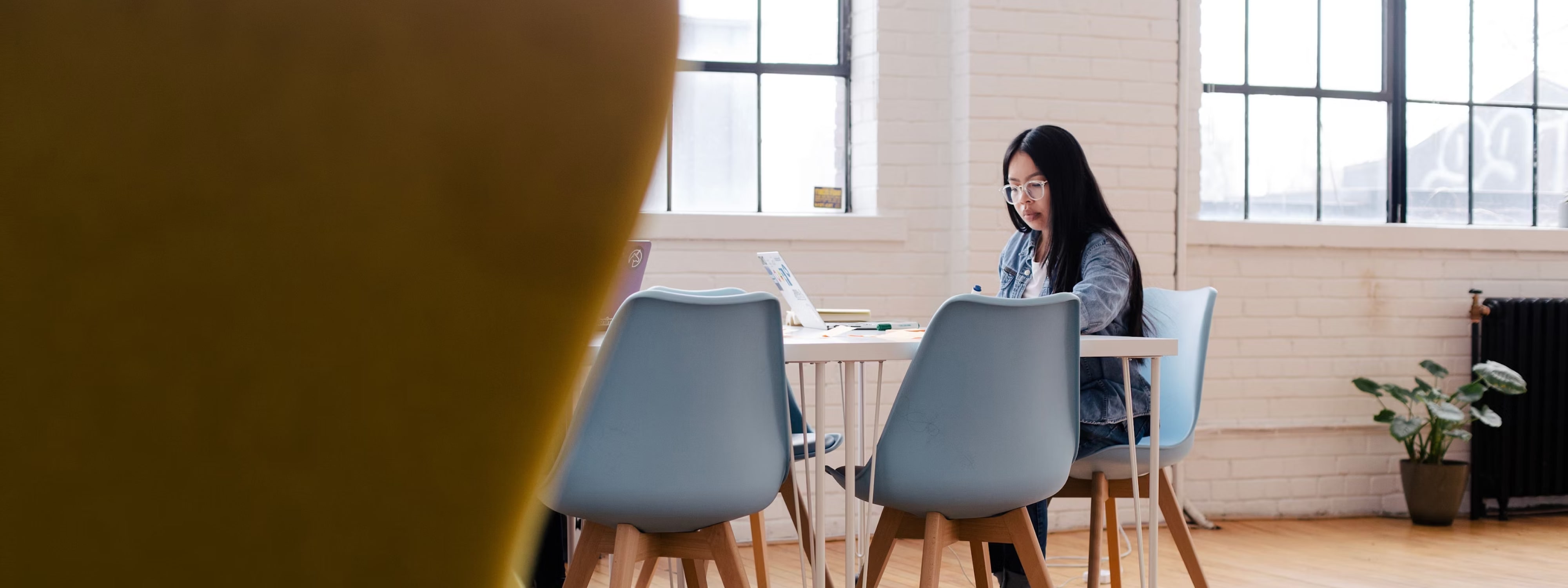 Woman working on laptop in bright, minimalist office with blue chairs